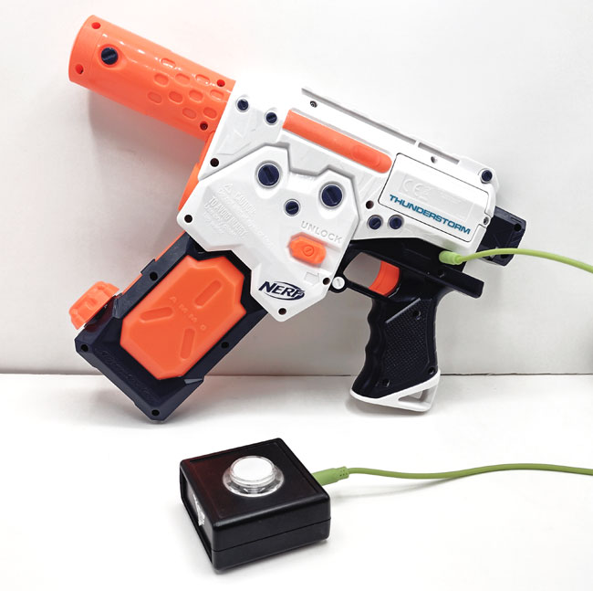 Switch adapted NERF Thunderstorm battery powered water pistol, standing up, with a small SANWA switch plugged in.