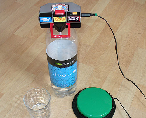 Switch Adapted drink dispenser, on top of a large Lemonade bottle by a glass and green accessibility switch.