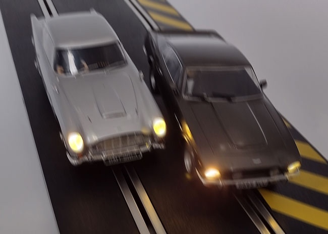 Blurry image of the two James Bond Scalextric Aston Martin cars racing.